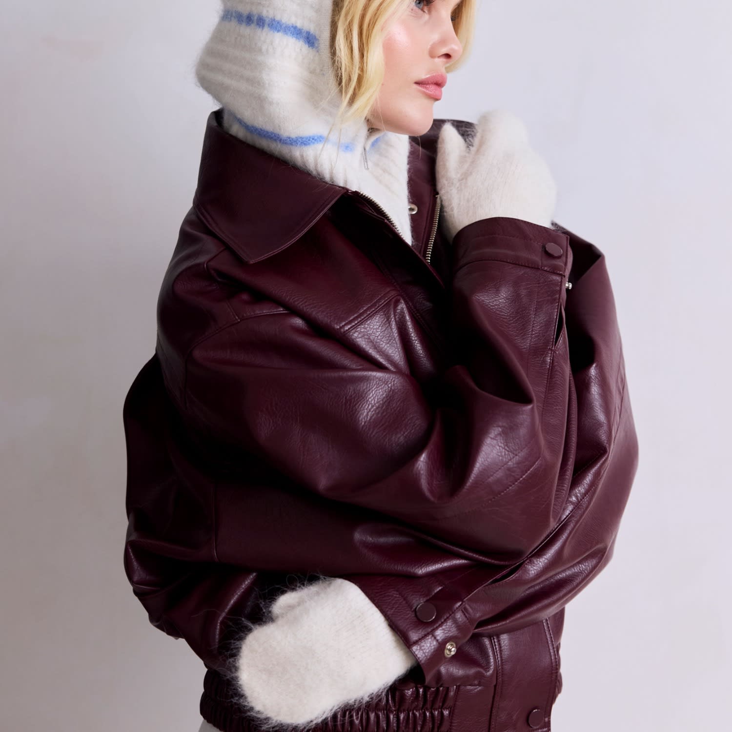 Model in a burgundy leather jacket wearing white Arctic Fox alpaca mittens