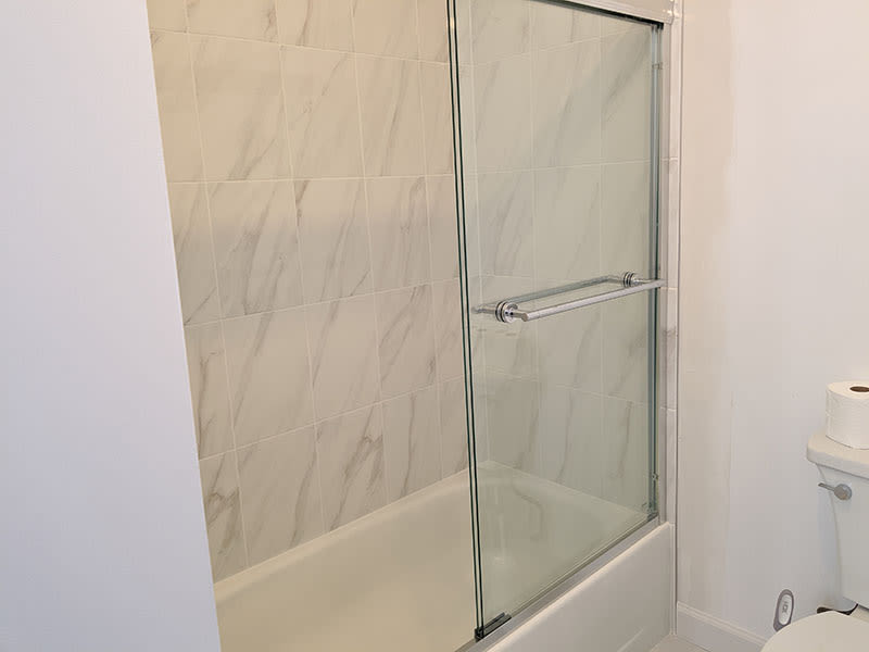 New bathtub with a marble-look tile surround and sliding glass shower door