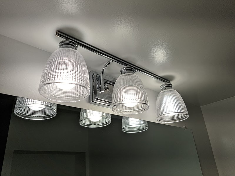 Four-bulb chrome vanity light with ribbed glass shades above the bathroom mirror