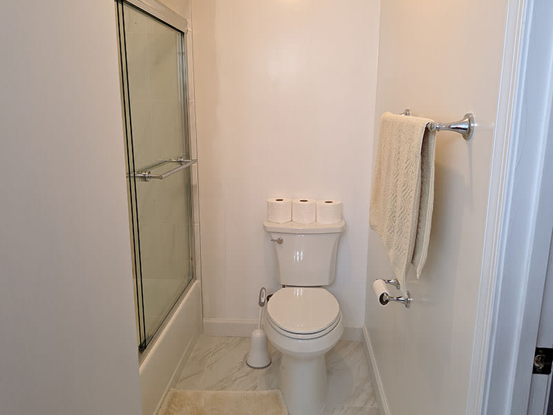 New toilet beside the tiled tub enclosure with a chrome towel bar