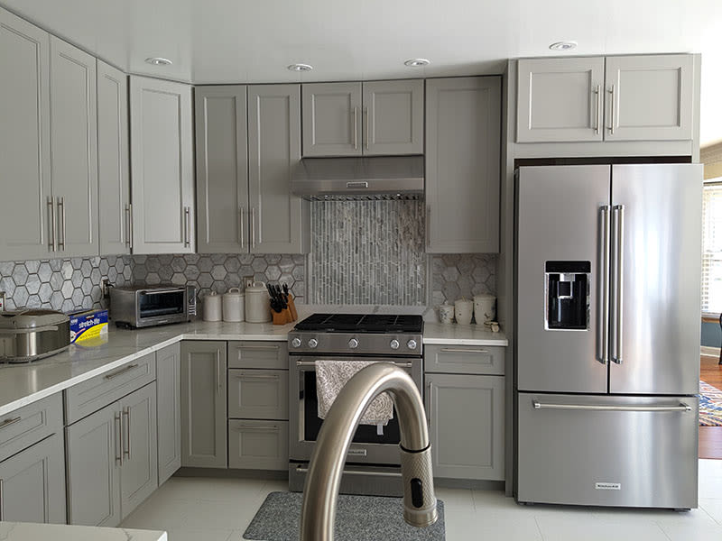 Grey shaker cabinets and a stainless gas range below a vertical glass tile accent