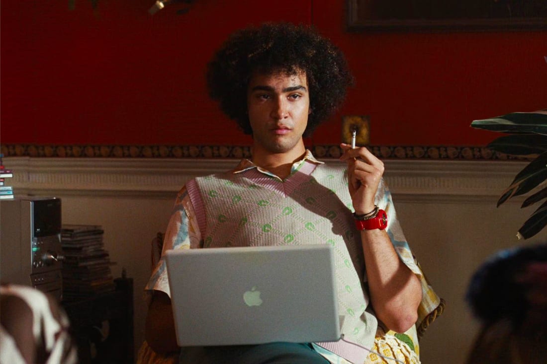 A man sitting in a chair holding a cigarette and a laptop