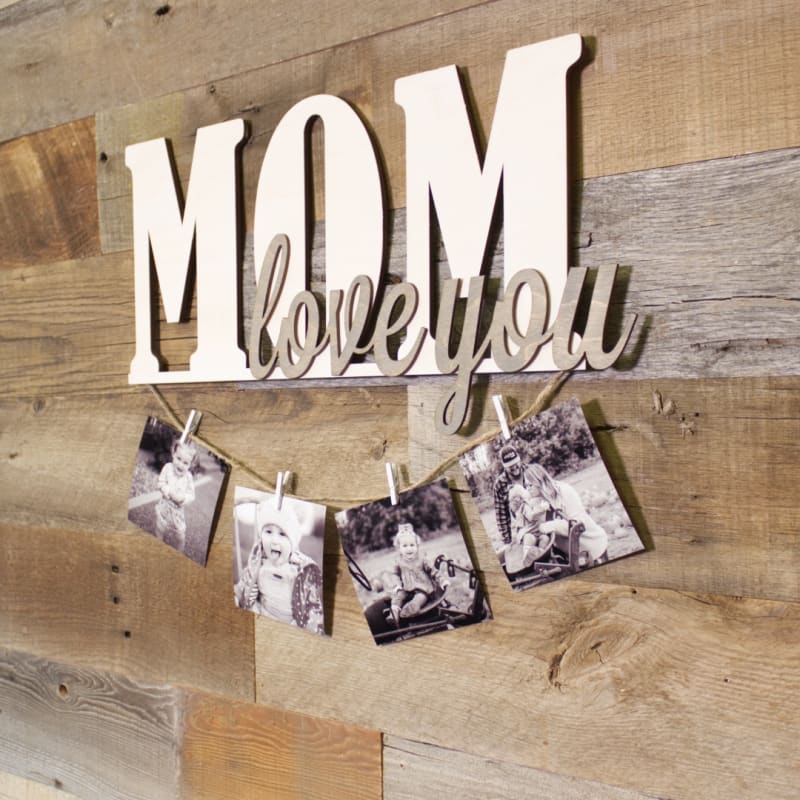 Image contains the words, “love you mom” cut from wood with a piece of twine hanging from them. Small clothespins hold four photos onto the twine.