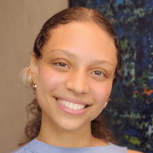 Portrait of a smiling young woman with curly hair pulled back, wearing a light blue top