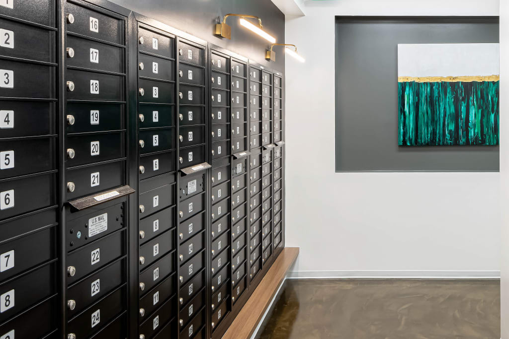 Sleek mailroom featuring numbered mailboxes, brass lighting, and modern wall art