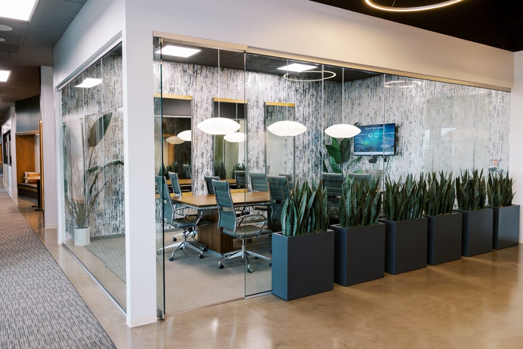 Modern office conference space with glass walls, stylish lights, and a row of tall indoor planters outside