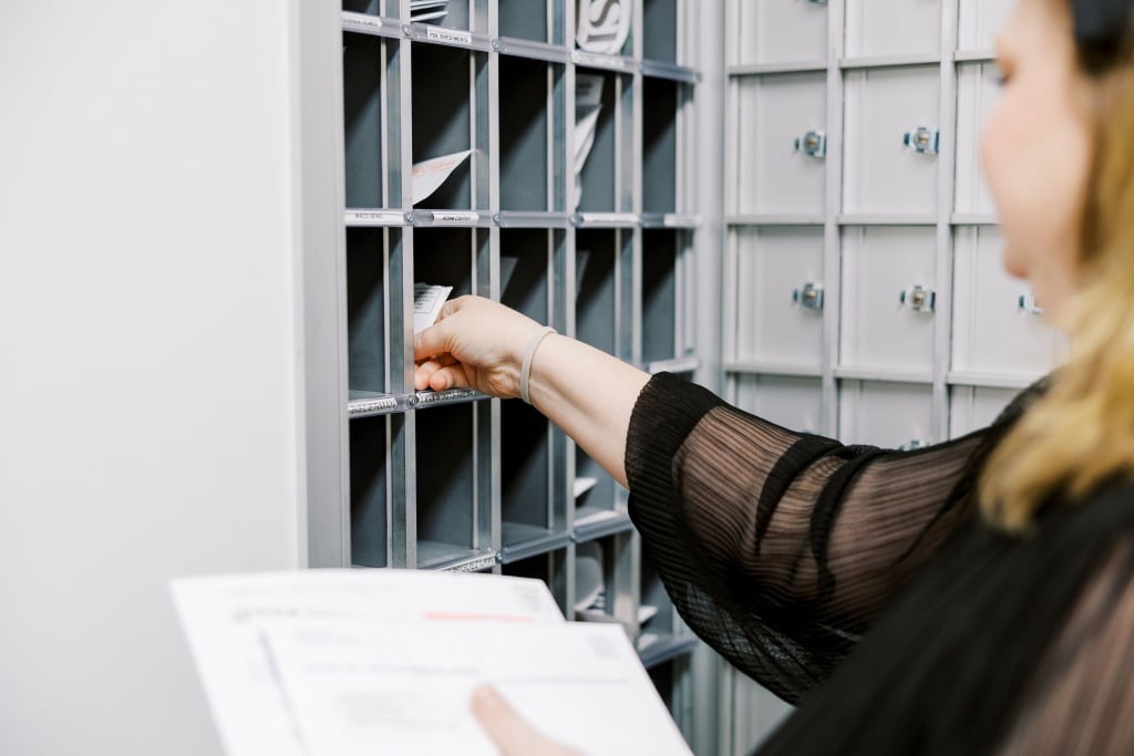 A close-up of a team member sorting envelopes into a wall of secure, open-front corporate mail slots in a Lucid Private Office mailroom.