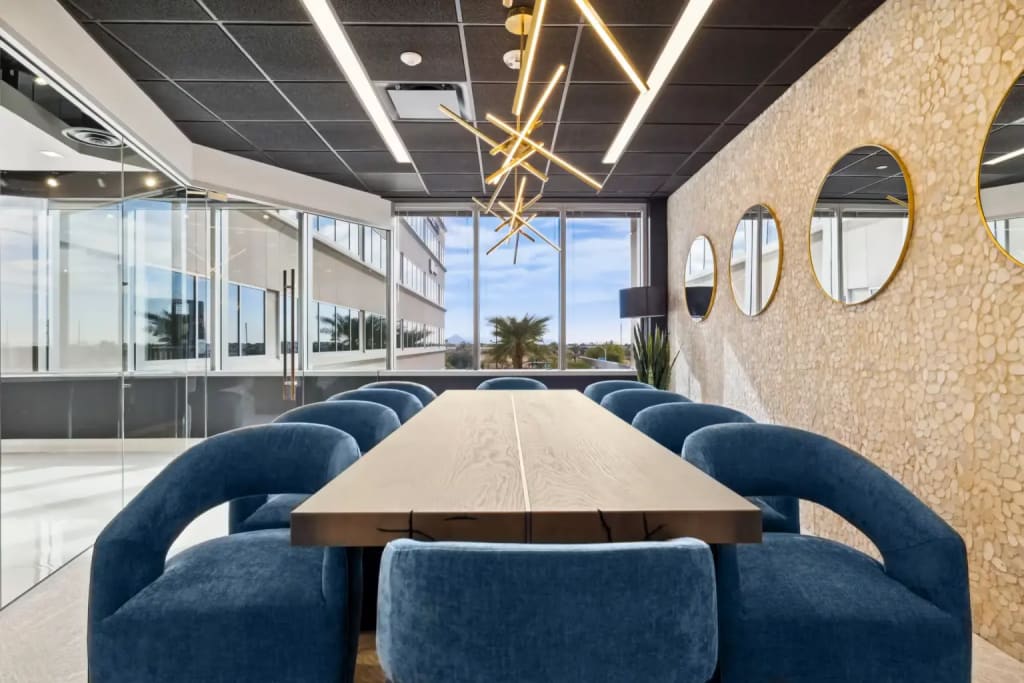 Boardroom: Lucid Private Offices conference room with live-edge wood table, blue velvet chairs, gold sunburst chandelier, and floor-to-ceiling windows.