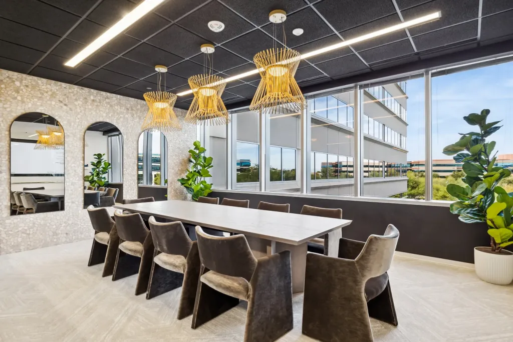 A luxury conference room at Lucid Private Office featuring a long light wood table surrounded by plush brown velvet armchairs, distinctive woven gold pendant lights, large windows, and arched mirrors.