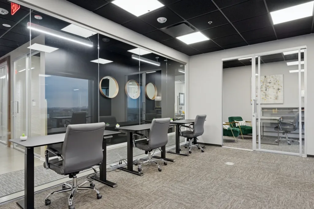 Shared executive suite at Lucid Private Office showcasing private desks equipped with individual grey rolling chairs on grey carpet, positioned next to floor-to-ceiling glass partition walls.