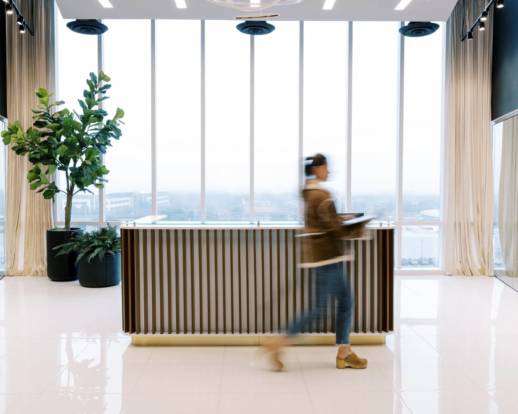 Woman walking past the reception desk at Lucid Private Offices - West Plano / Willow Bend