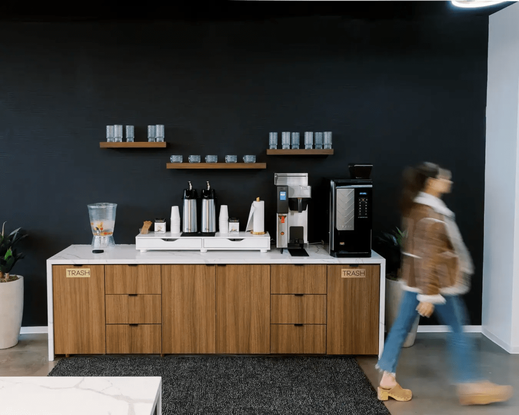 Coffee bar: Lucid Private Offices coffee bar with espresso machine, glassware shelves, and complimentary beverage service against a black accent wall.