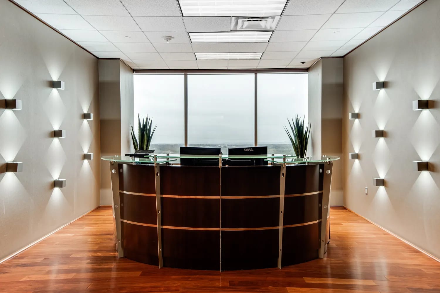 Elegant Lucid Private Offices reception desk with curved dark wood paneling, glass top, and warm wall lighting
