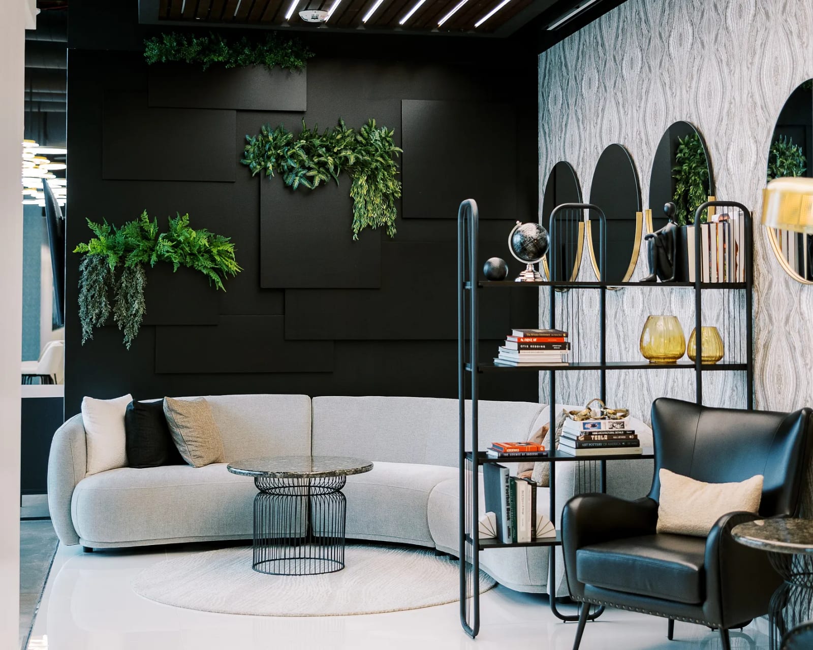 Contemporary lounge area with dark walls, circular mirror decor, plants, and white accent chairs