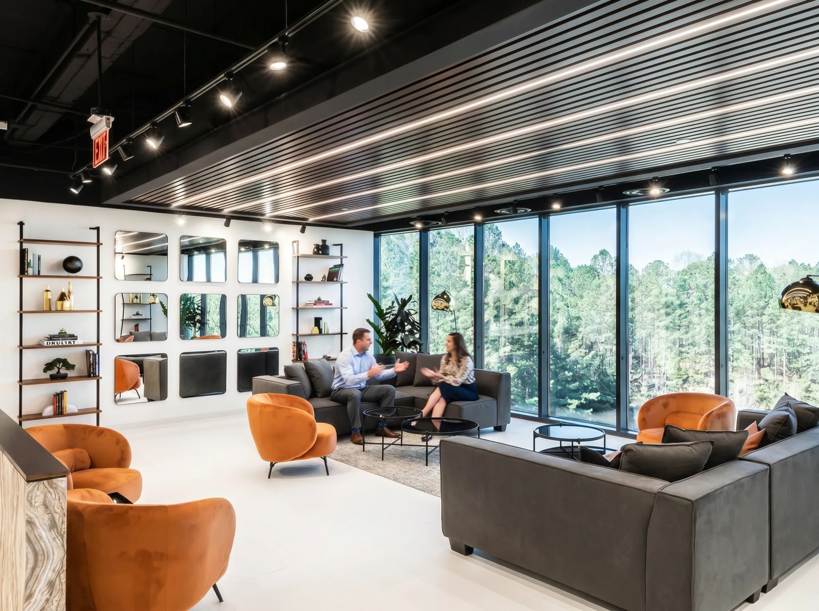 Reception lounge with orange velvet chairs, grey sofas, and dramatic slatted ceiling overlooking greenery