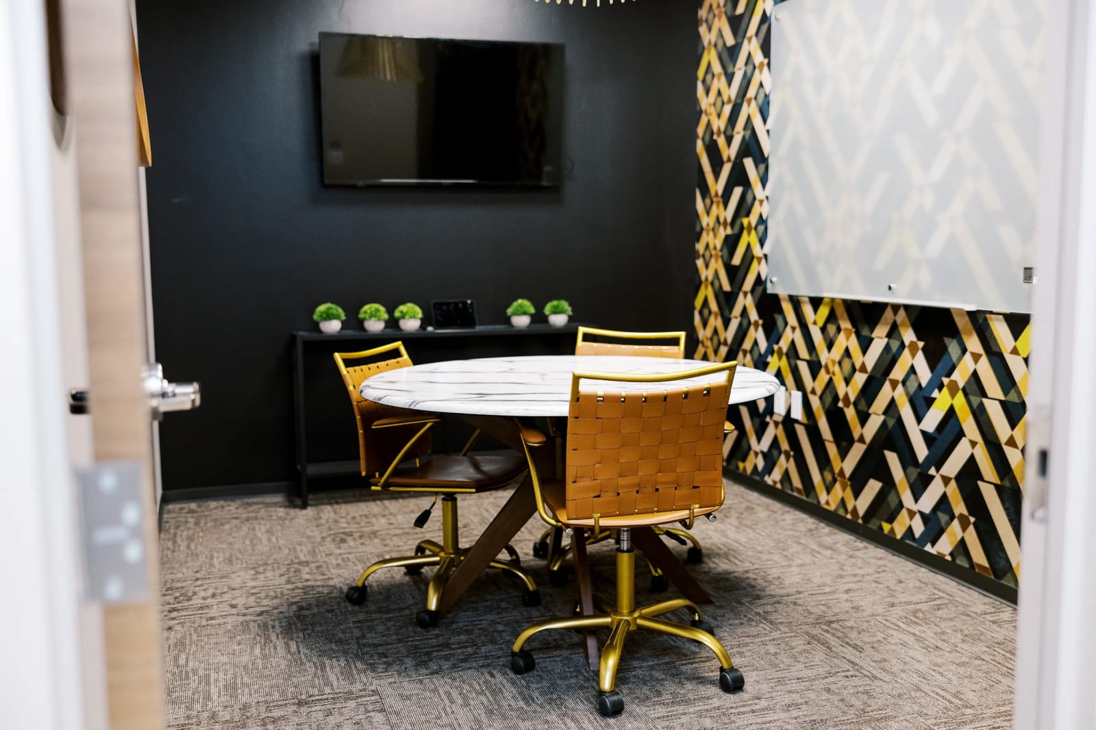 Small meeting room with a round table, gold-toned chairs, and bold geometric patterned wall