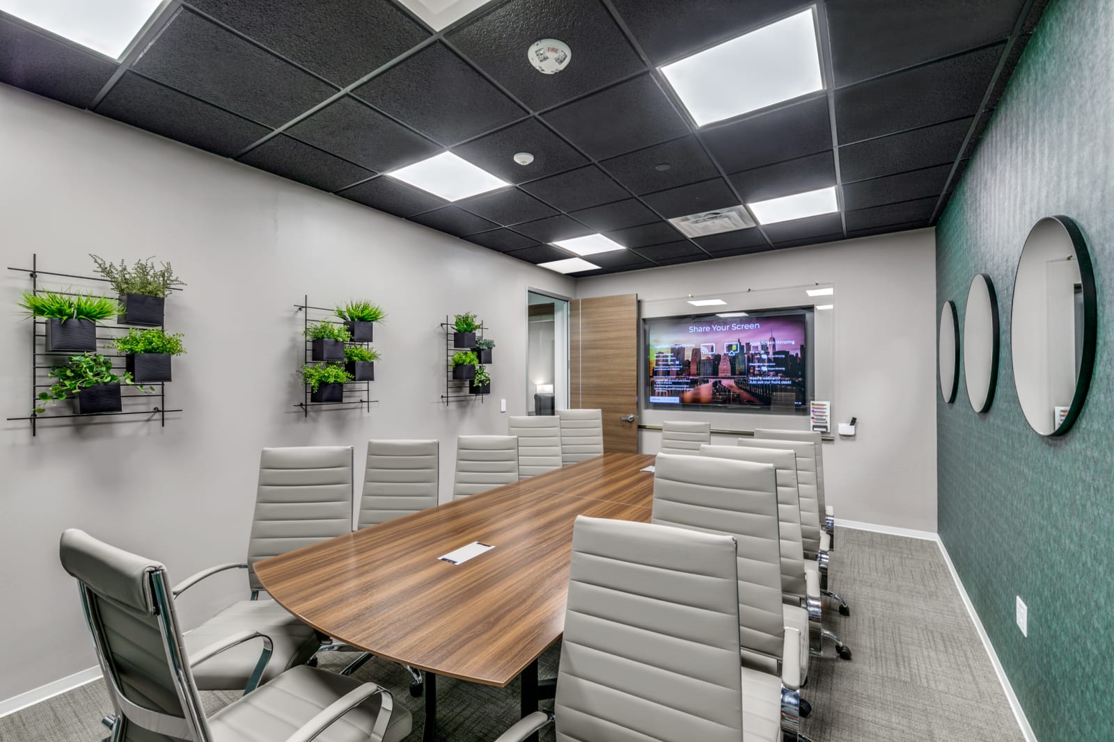 Small Lucid Private Offices conference room with wood table, gray chairs, and wall-mounted display
