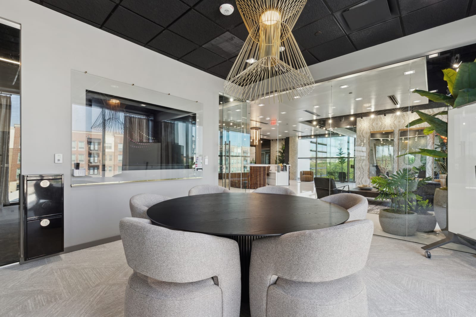 Modern meeting area with a round table, gray chairs, glass walls, and contemporary lighting.