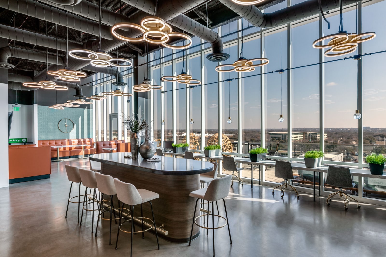 Coworking lounge at Lucid Private Offices West Plano with communal table seating, pendant lighting, and floor-to-ceiling skyline views