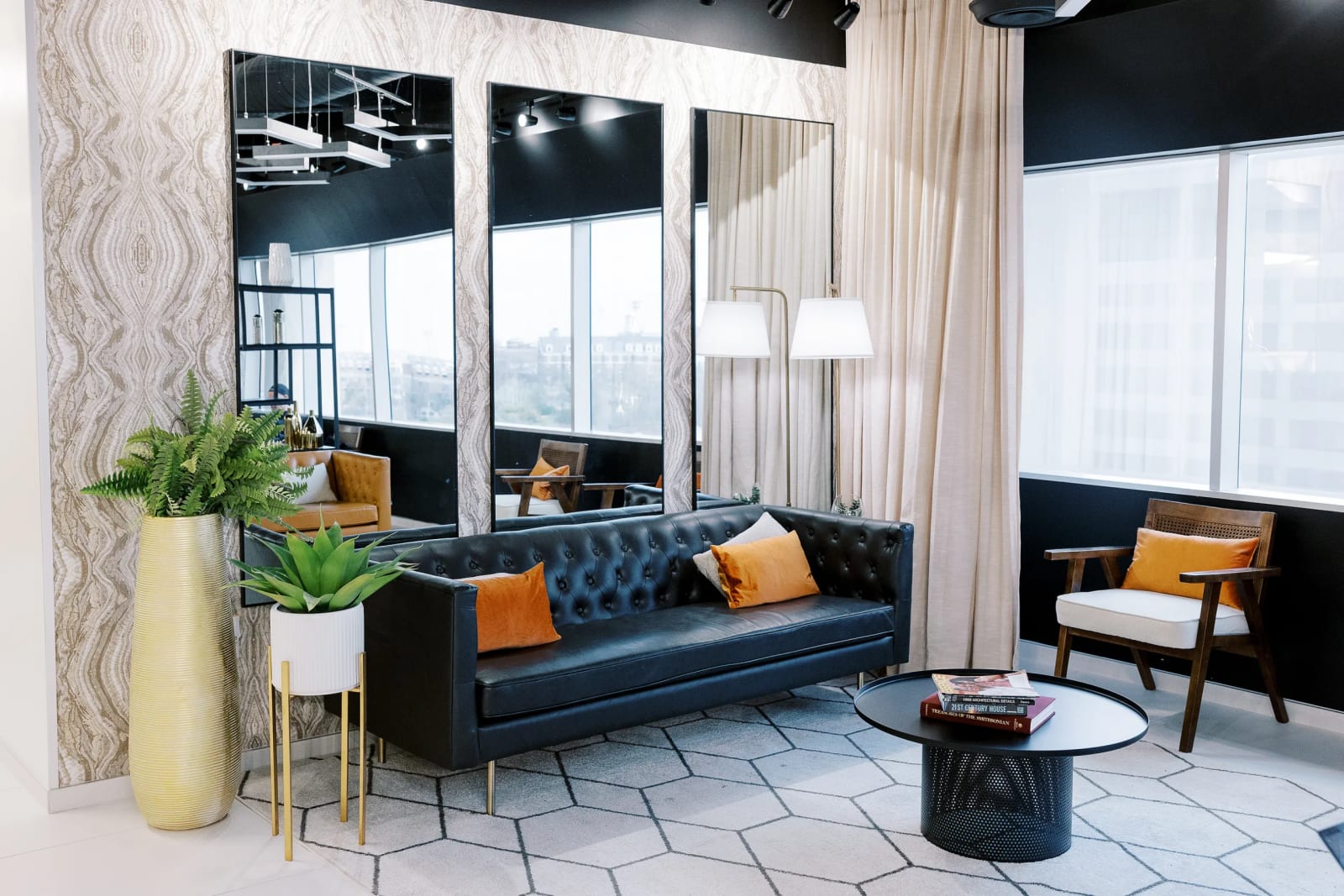 Modern lounge seating area with a navy blue sofa, floor lamp, tall plant, and large windows