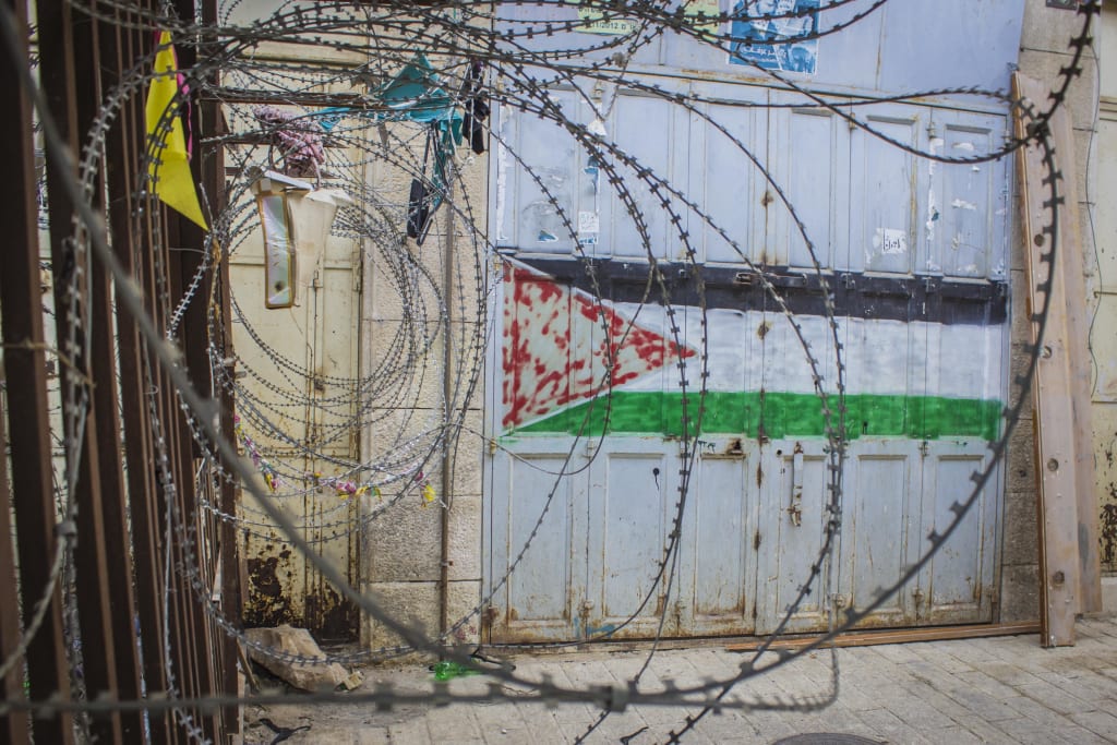 bandeira da Palestina pintada em muro e alguns arames farpados perto 