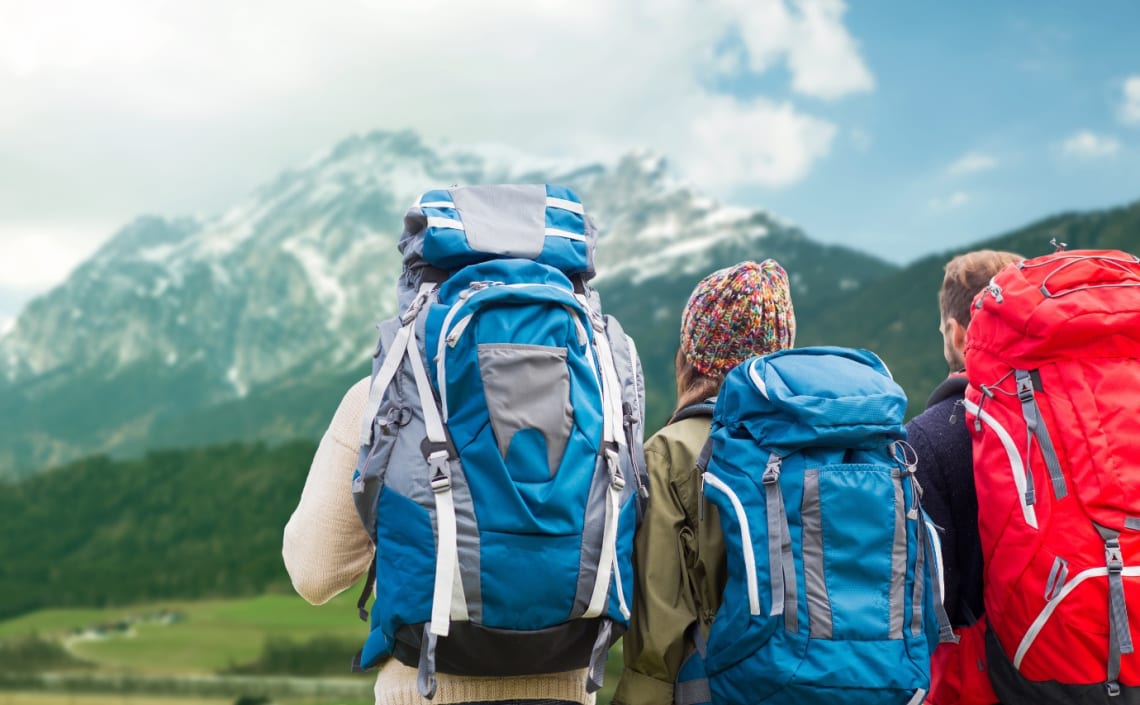 Dos chicos y una chica con mochilas mirando hacia la montaña