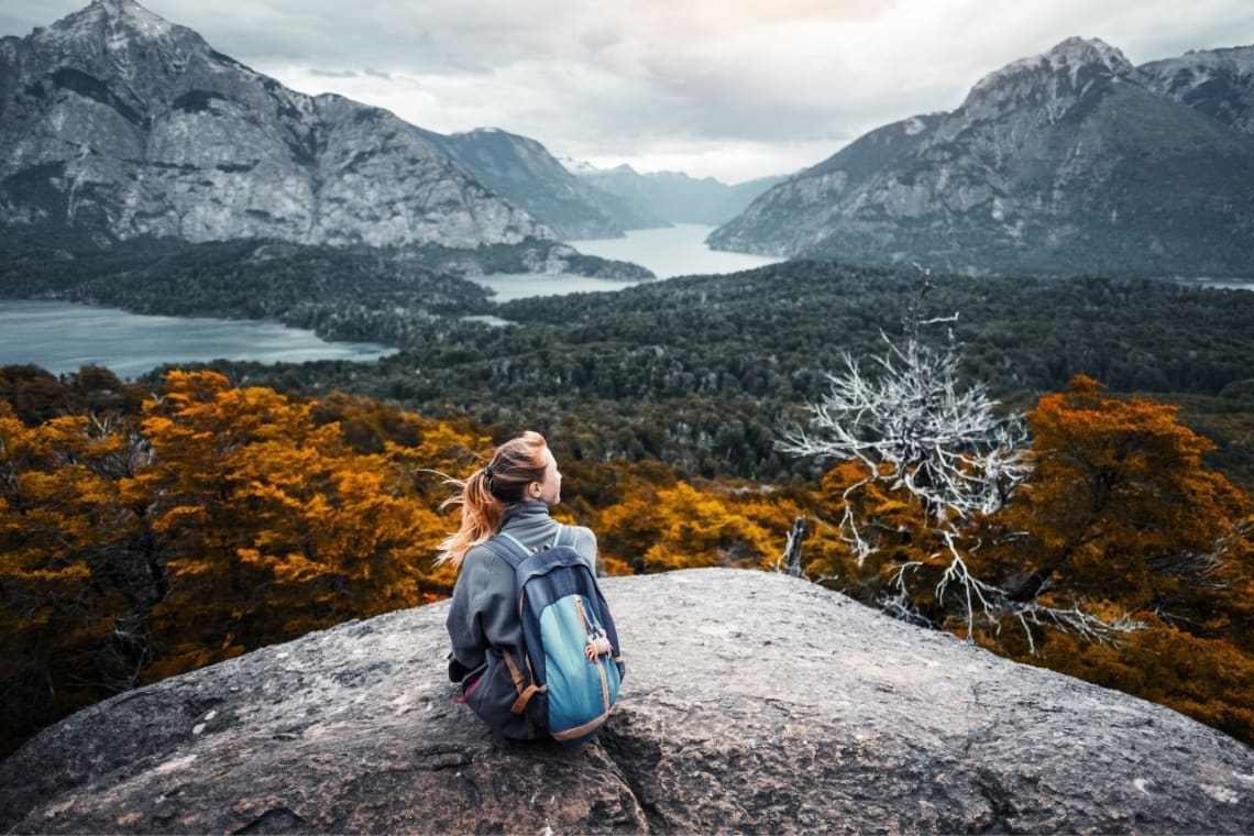 Chica descansando sobre una piedra con vista los bosques de Bariloche