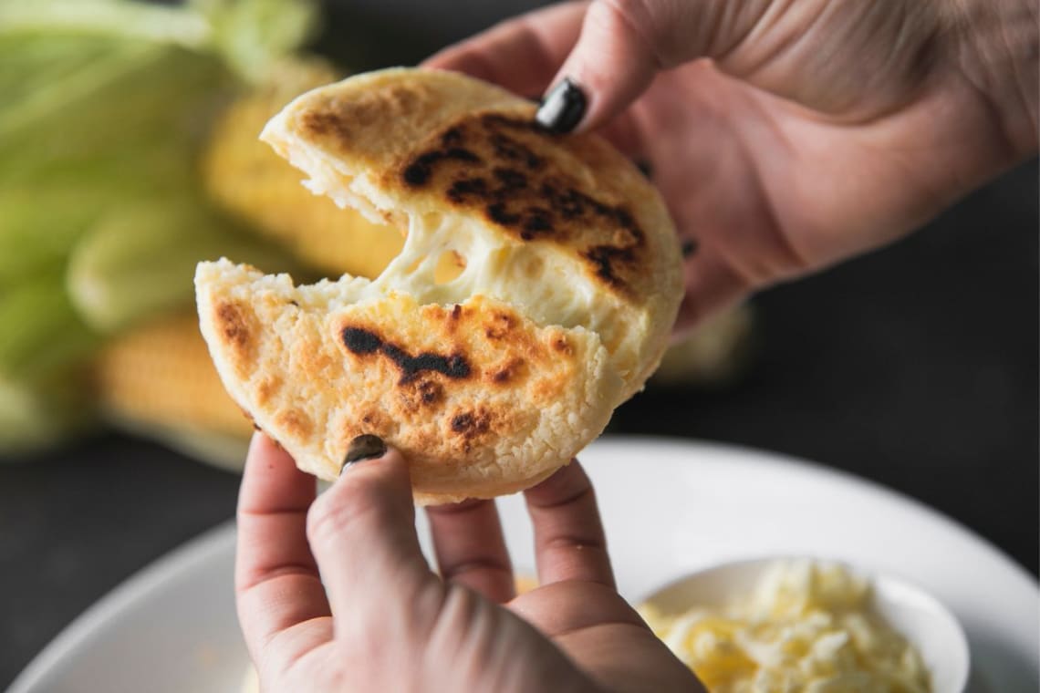 Manos de mujer abriendo una arepa rellena de queso