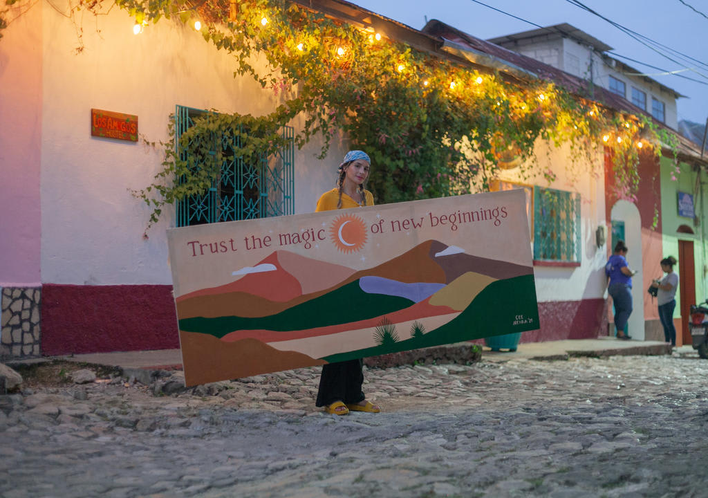 Young girl holding a painting that says: "Trust the magic of new beginnings" in a colonial street of Guatemala