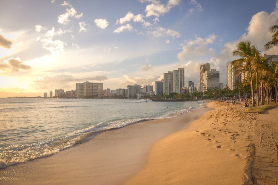 Viaje a Hawaii precio: playa al atardecer con edificios a lo lejos