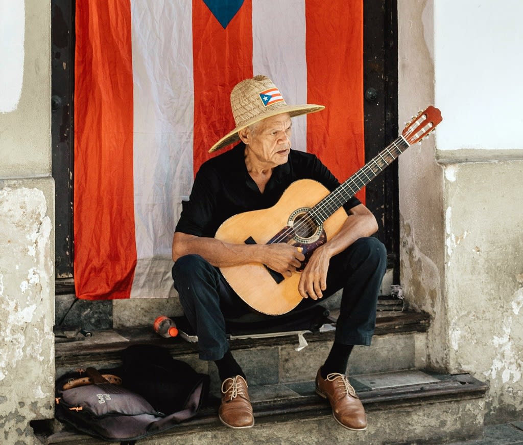 Street performer with a guitar seated in the steps of an old house in San Juan