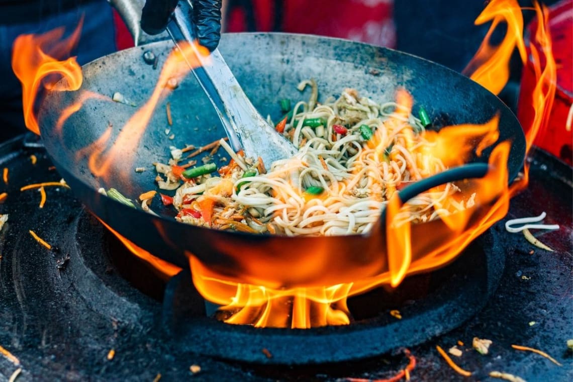 Saltando fideos en wok con llama de fuego