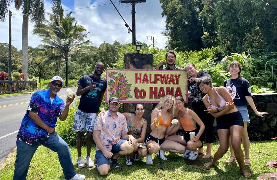 Group of young travelers posing for a picture with the "Halfway to Hana" sign in Maui, Hawaii