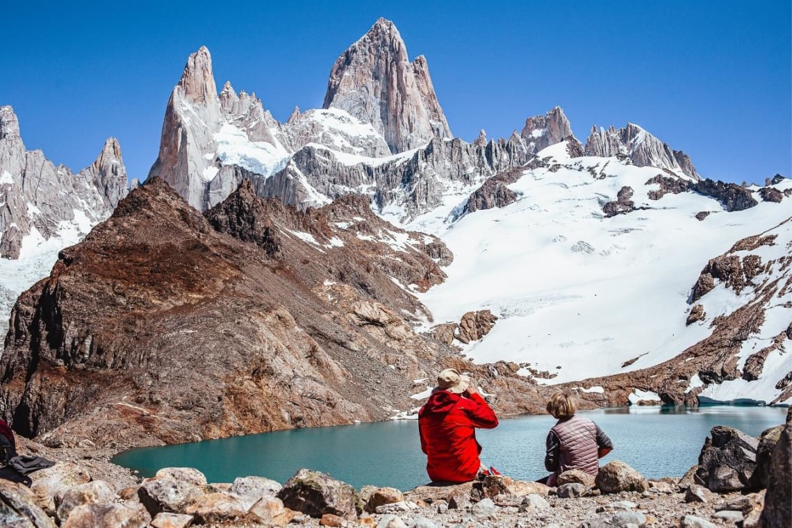 Dos caminantes descansan frente a la Laguna de los Tres con vista al Cerro Fitz Roy, en El Chaltén