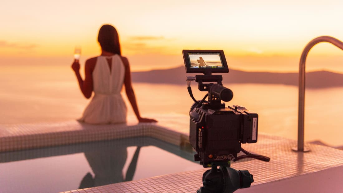 Camera filming a travel influencer watching a sunset by the pool