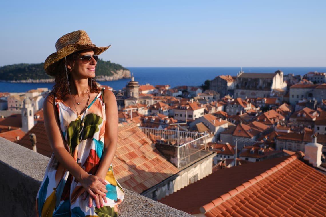 Smiling girl looking at Dubrovnik's old town from a viewpoint at sunset