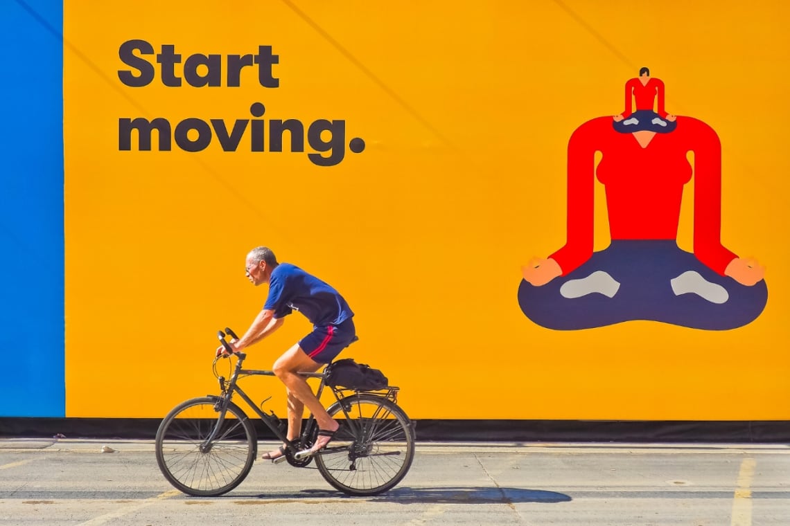 Hombre pasando en bicicleta por delante de cartel que dice "Start moving"