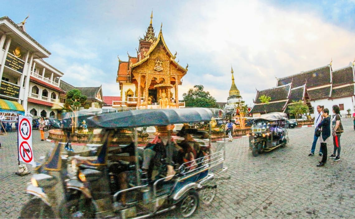 Tuk tuks pasando por adelante de un templo de Tailandia