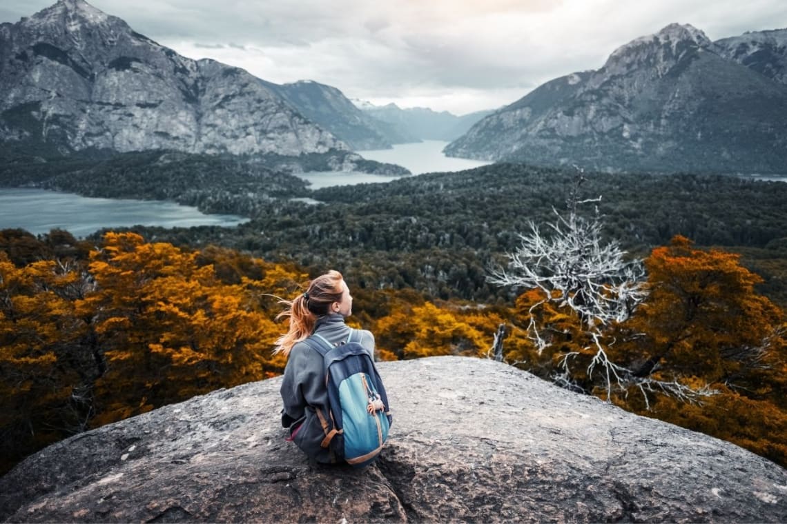 Chica sentada sobre una roca con vista panorámica a bosque, lagos y montañas en el Parque Nacional Nahuel Huapi