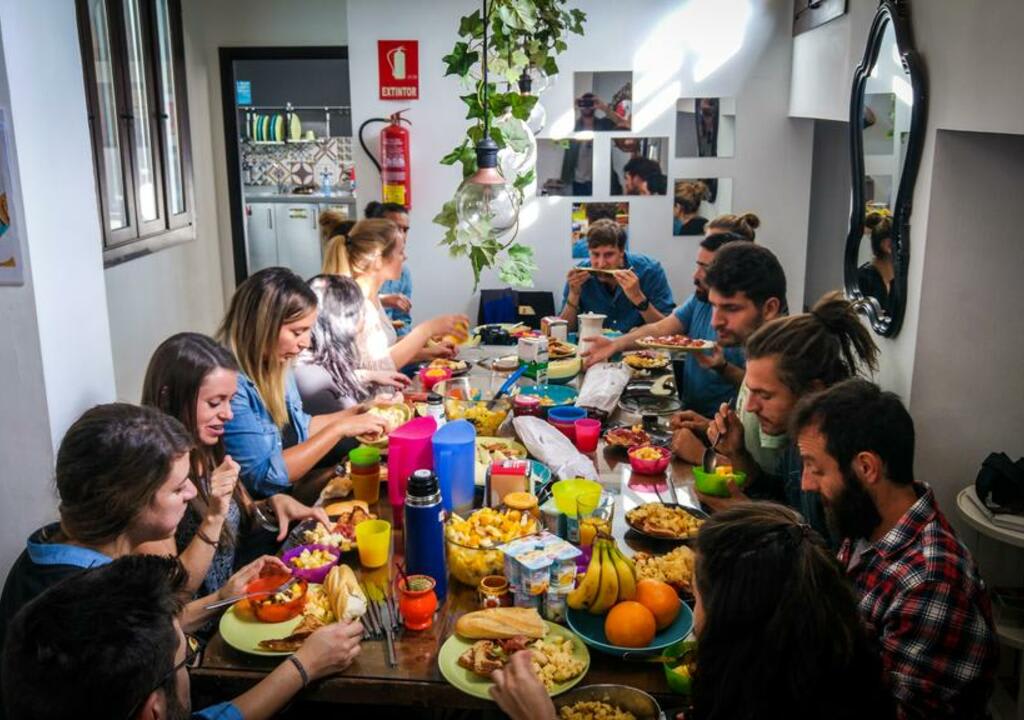 Gran grupo de voluntarios comiendo en una mesa de hostel llena de comida