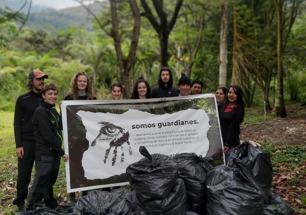 Vida sostenible: voluntarios de proyecto ecológico mostrando cartel que dice "somos guardianes", refiriéndose a su trabajo ambiental en la selva