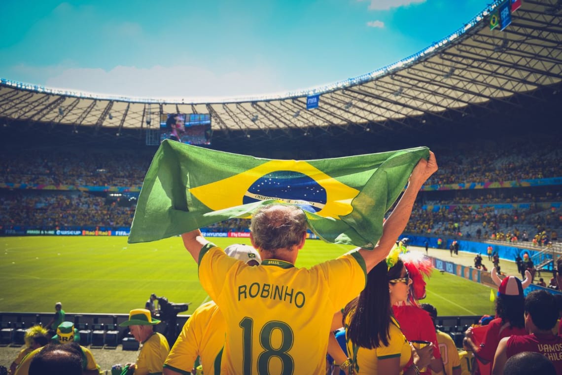 Hincha de Brasil en estadio de fútbol levantando una bandera de su país
