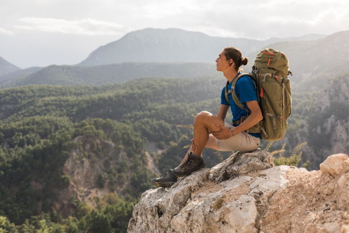 Joven con mochila en una roca mirando la naturaleza desde lo alto