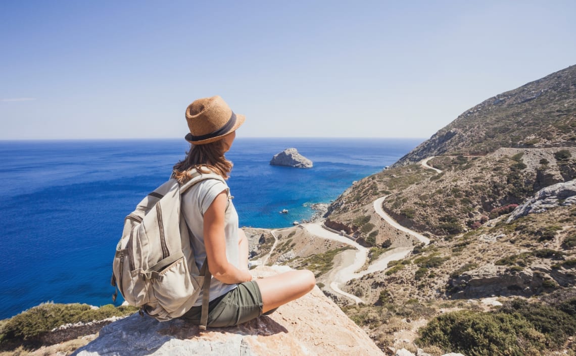 Viajera sentada mirando paisaje de montaña y mar desde lo alto