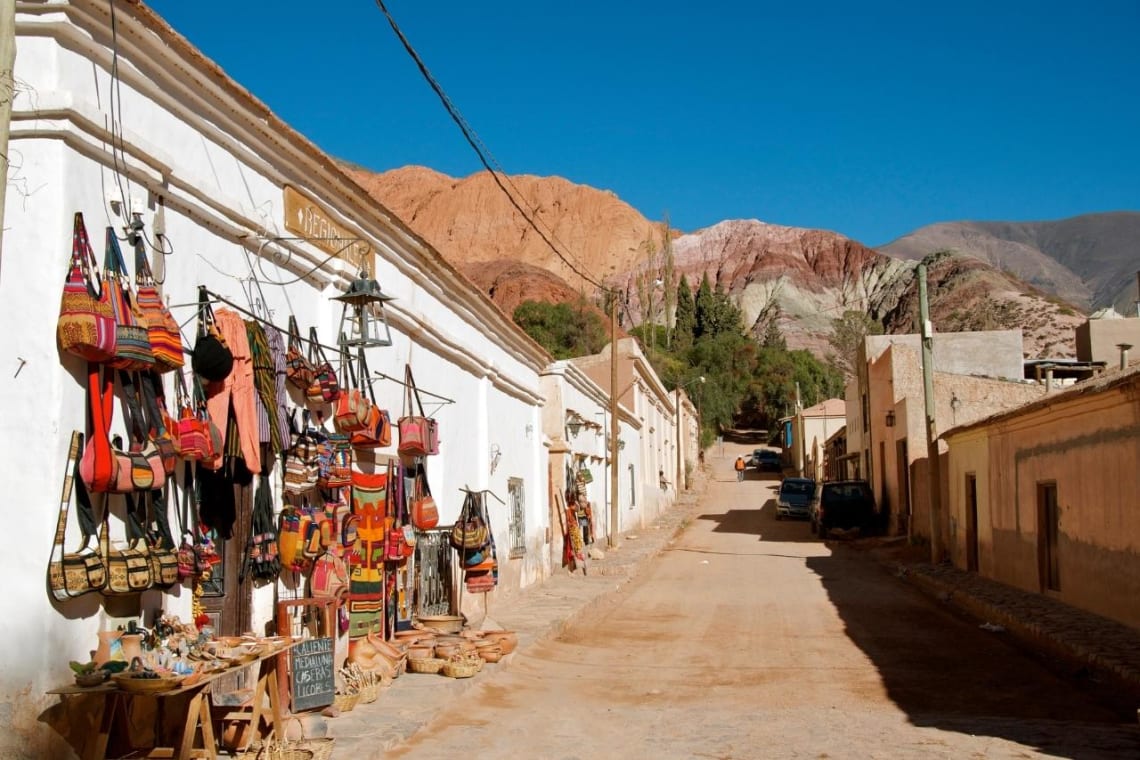 Calle de tierra y construcciones bajas de adobe con Cerro de los 7 colores de fondo. Purmamarca, Jujuy