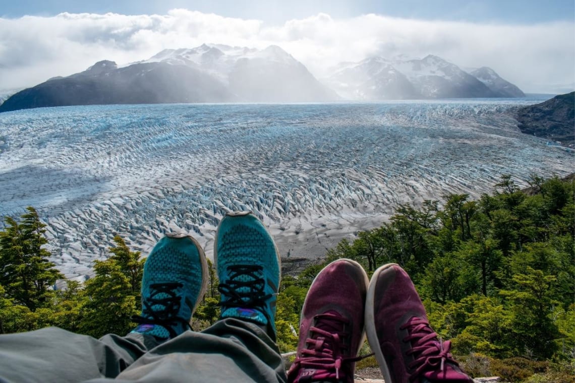 Piernas estiradas de una pareja descansando frente a un glaciar. Parte del Circuito W
