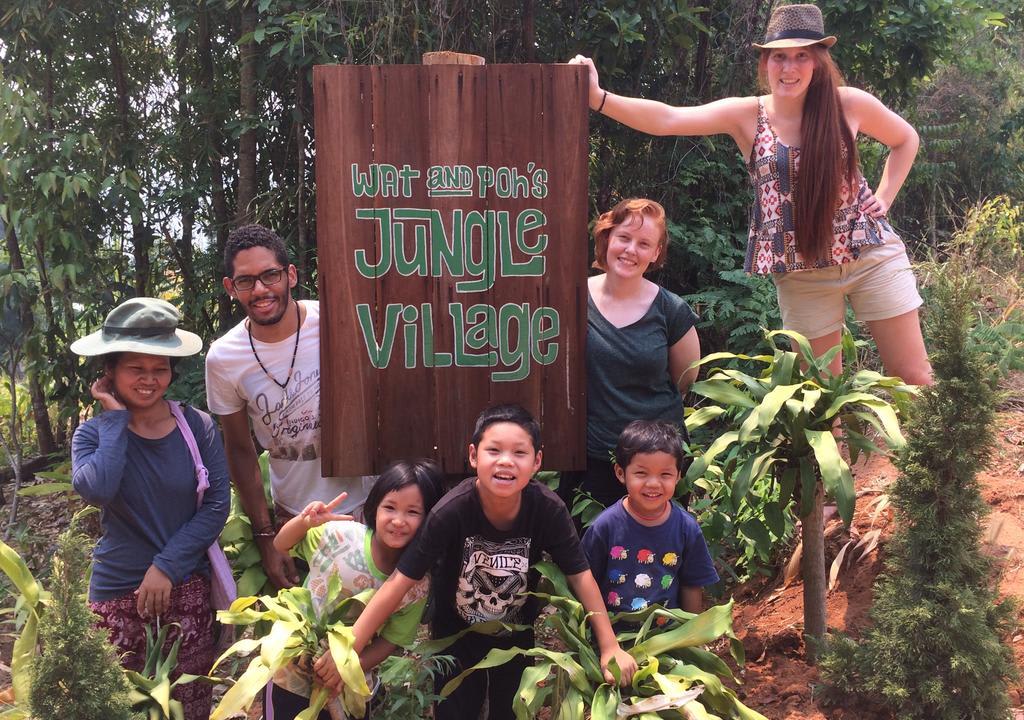 Volunteers with kids in a farm in front of a sign that reads "Jungle Village"