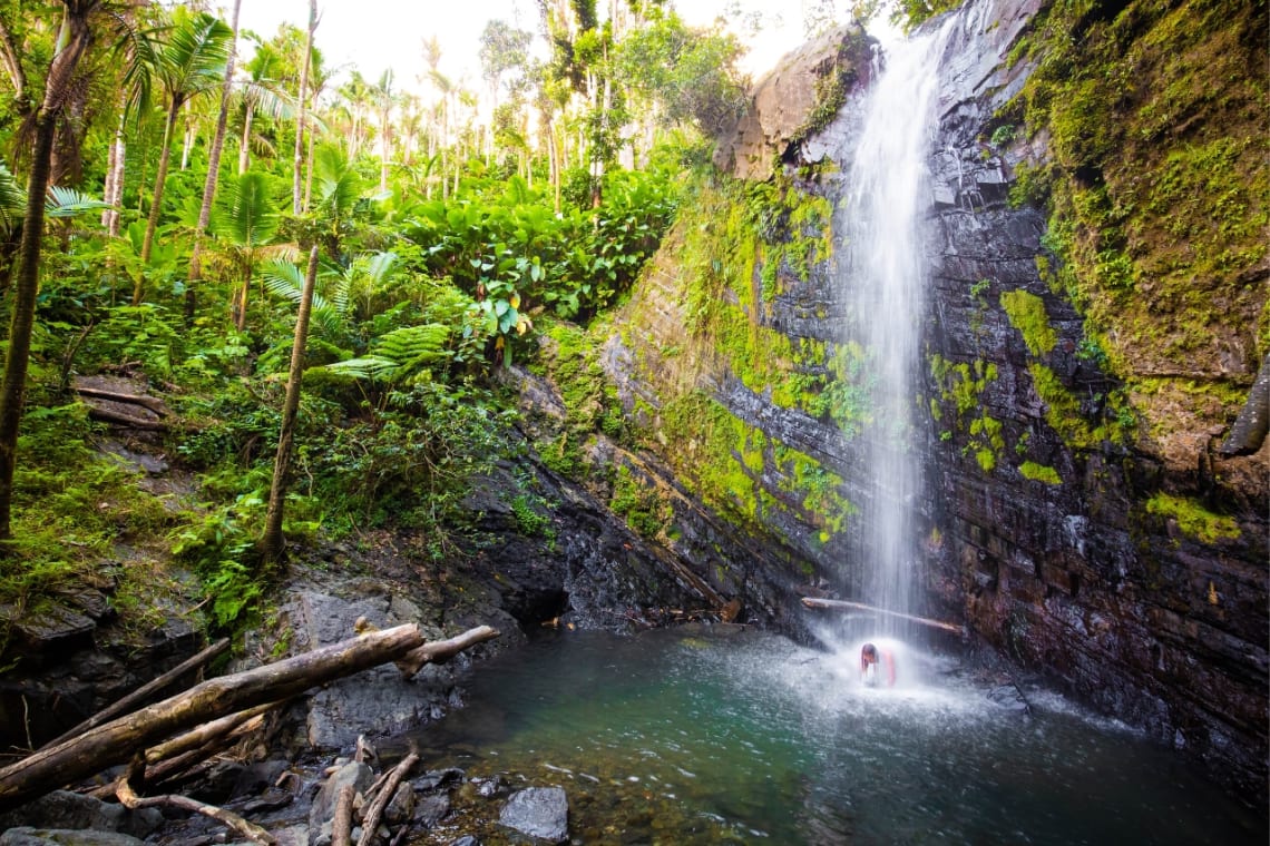 Chica bañándose en una cascada de El Yunque, un destino de ecoturismo