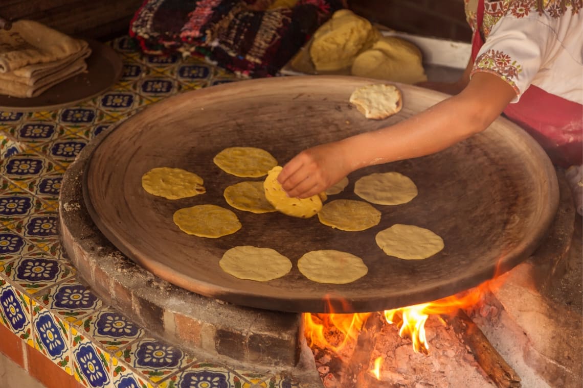 Mujer cocinando tortillas de maíz sobre plato de barro al fuego