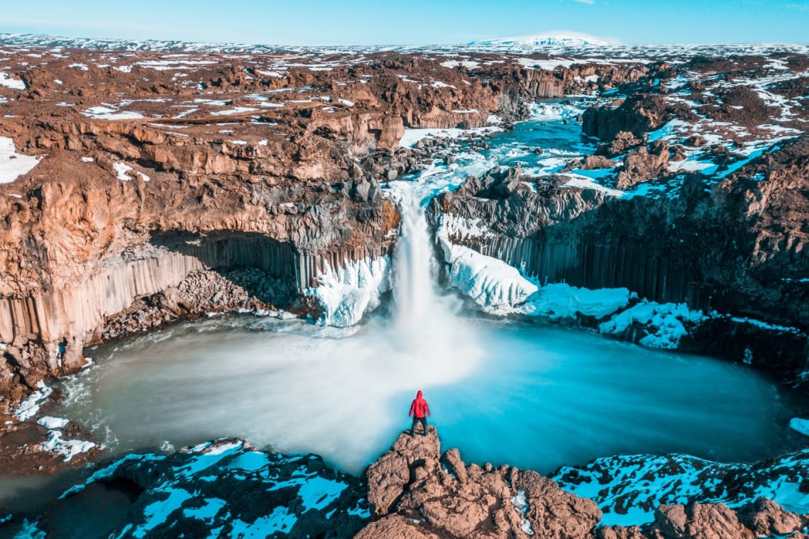 Viajero en una alta roca mirando cascada nevada en Islandia
